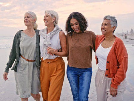 Four joyful women walking arm in arm on the beach at sunset.