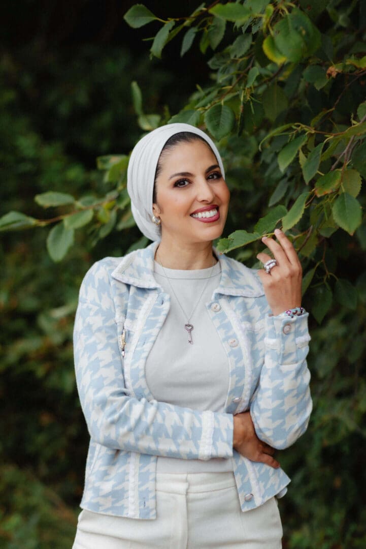 Smiling woman in a white hijab and checkered jacket outdoors.
