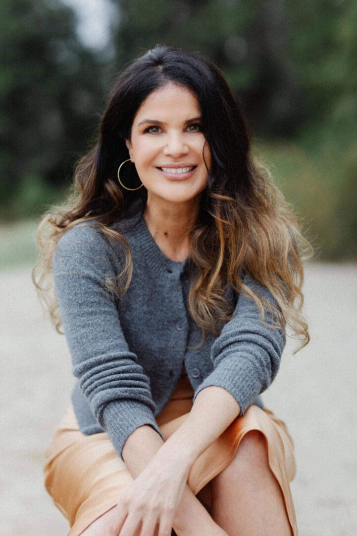 Smiling woman with long hair in a gray sweater outdoors.